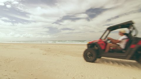 An All Terrain Vehicle driving along a beach near an ocean in Australia with cloudy natural lighting. Wide shot on 4k RED camera.