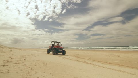 An All Terrain Vehicle driving along a beach near an ocean in Australia with cloudy natural lighting. Wide shot on 4k RED camera.