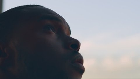 Handsome, young, black man stands on a balcony and looks into the distance over a small bay with clear water, in deep thought in natural daylight, in Australia. Medium shot in 4K on a RED camera