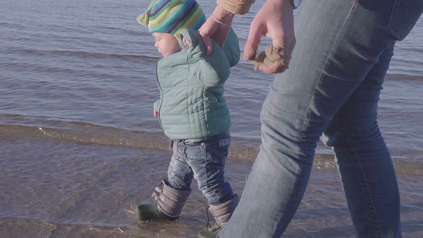 Mom with a little kid walks along the spring beach