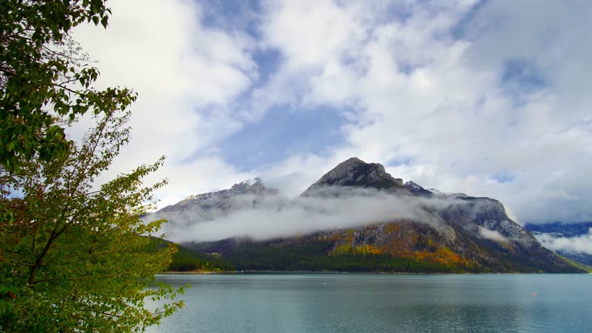 Lake Minnewanka cloudscape timelapse panning panoramic view with snow mountain and forest in Banff National Park.