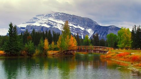 Wood bridge snow mountain and autumn foliage over lake with ripple in Banff National Park, Canada.