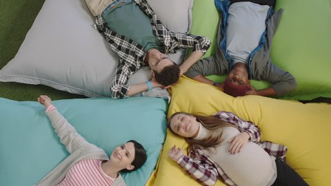 top view happy group of business people jumping on colorful pillows resting together exhausted after working relaxing diverse colleagues smiling enjoying creative office workplace