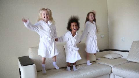 Three little girls are jumping on the couch.
Girls of different nationalities in white coats dance and laugh after a bath.