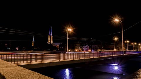 Time lapse video recorded in Wroclaw, Poland. Blurred traffic, city by night, cathedral towers in the background. A lot of light points, street lamps with flares. 