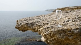 Red wine is poured into a glass on a background of rocky sea shore. A hand with a bottle pours wine into a glass standing on a rocky seashore