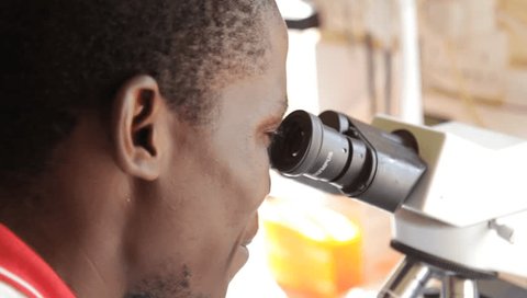 Uganda. 2017/5/11. A laboratory technician is viewing a blood smear specimen under a light microscope.