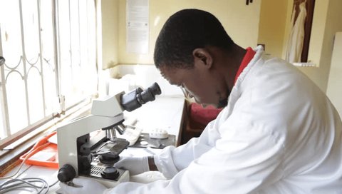 Uganda. 2017/5/11. A laboratory technician is viewing a blood smear specimen under a light microscope.