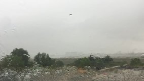 Heavy rain falls on a car windscreen with blurry background