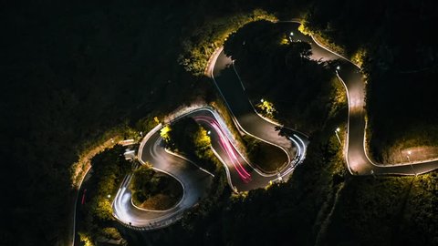 Hyperlapse of elevated view cars driving on beautiful S curved road in mountains at night, Keelung Mountain. Aerial timelapse of hillside roads through forest with turns at evening. Jiufen journey-Dan