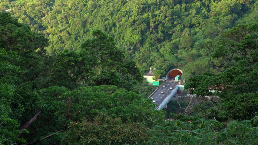 4K, Aerial of tunnel in freeway with cars traffic driving through mountain of Taipei city. Beauty elevated view of road with green trees at Taiwan. Landscape with mountains at day time of summer-Dan