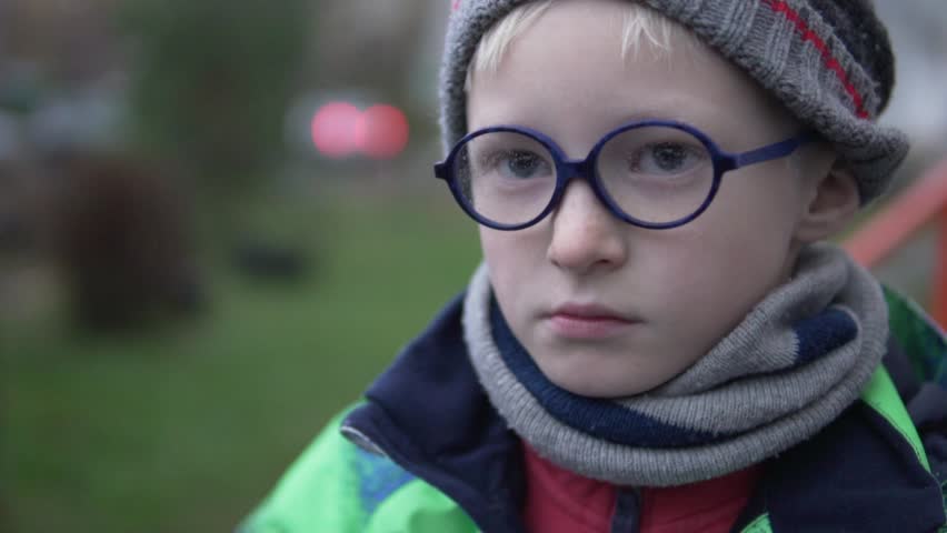 Close-up of a boy with glasses. He stands on the street, wearing a drop of rain glasses. The boy is warmly dressed. The child smiles and finger tightens glasses to his nose