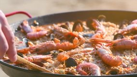 Paella traditional Spanish food, seafood paella in the fry pan with mussels, king prawns, langoustine and haddock. Person cooking paella outside. Sea food. Slow motion 4K UHD video