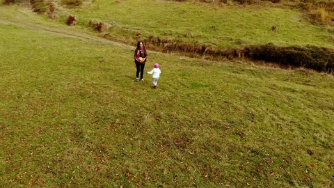 A young mother plays with her little daughter in the autumn forest. Mom with a little beautiful girl playing ball. Shooting from the quadcopter.