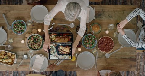 happy family preparing delicious thanksgiving lunch grandmother taking photo of turkey using tablet sharing celebration enjoying homemade meal together overhead tracking