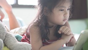 Asian child cute or kid girl sleep watch or looking tablet or smartphone for vdo clip or cartoon and playing the game very concentrate which causes ADHD or Hyperactive on bed in bedroom and morning