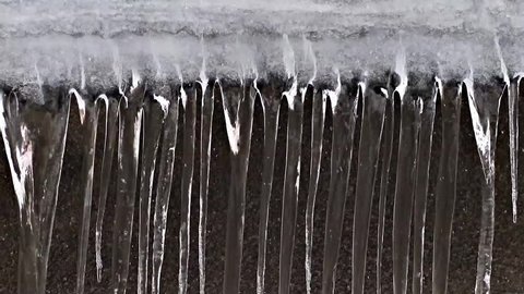 Dangerous icicles hang from the snowy roof of the house. Line of big icicles in the streets of the winter city.