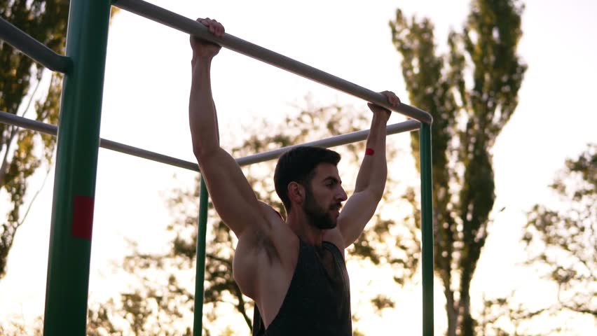 Pull-up strength training exercise - fitness man working out his arm muscles on outdoor gym doing chin-ups pull-ups as part of a crossfit workout work