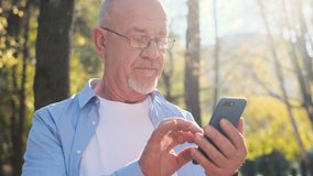 Portrait of senior man using mobile phone, holding device, texting, surfing internet, and using app. Senior man with a beard and wearing glasses looking at camera, smiling while rest in the park - Powered by Shutterstock - Get 15% off with code: PIKWIZARD15