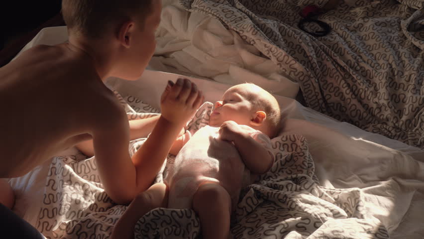 Slow motion shot of elder brother with baby sister on bed at home. 