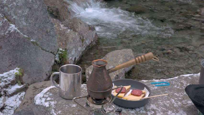 On a portable gas burner there is a kettle. Coffee is thrown into it. Picnic near the mountain river. Close-up