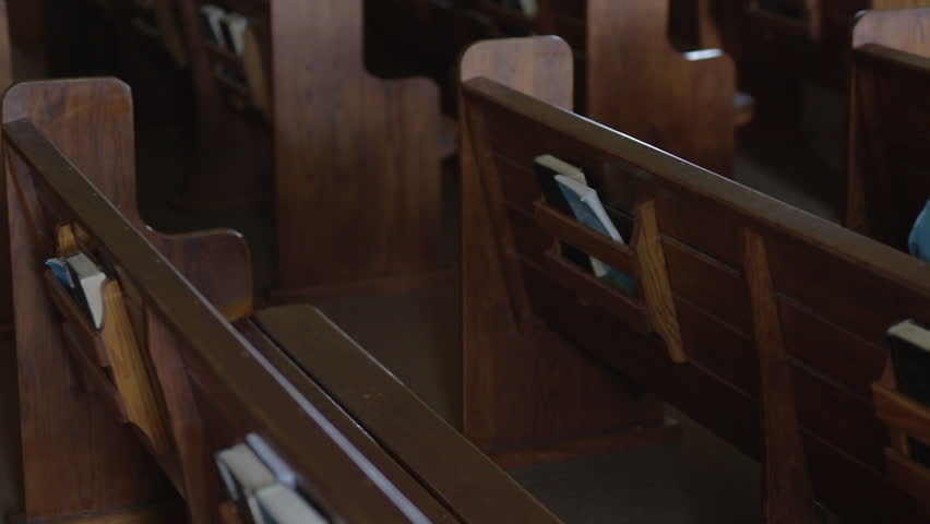 A Mennonite woman sits in an empty church pew and flips through a hymnal. | Shutterstock HD Video #1018931185
