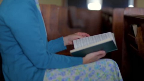 A Mennonite woman sits in an empty church and flips through the pages of a hymnal.