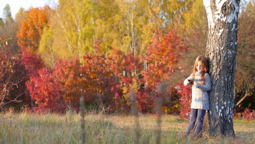 beautiful girl playing in the autumn park, blowing bubbles and having fun