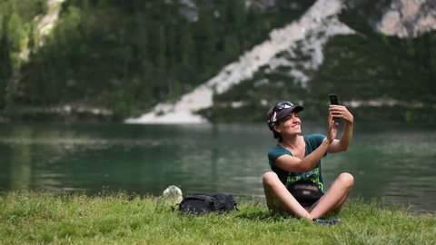 Young woman taking a self portrait with her smartphone by the lake, Lago Di Braies, Italy