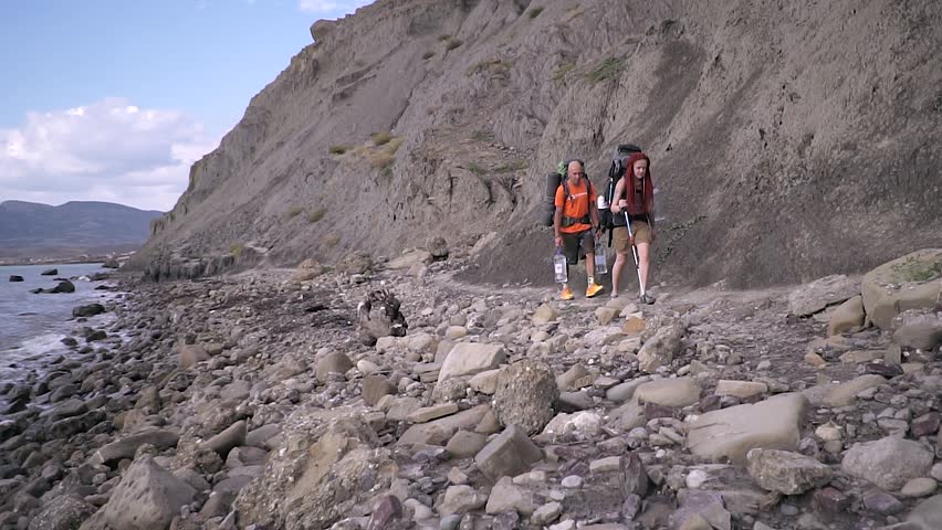 Active tourism. Travelers go hiking on a rocky seashore. Slow motion.