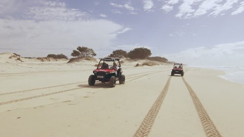 Two ATV vehicles racing on a beautiful beach with ocean and open sky in the background in Australia. Wide angle on 4k RED camera.