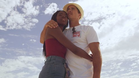 Young couple walking up to the top of a sand dune embracing each other in love, pointing and looking at scenic view and wide open sky in the background in Australia. Medium close up on 4k RED camera.