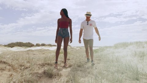 Young attractive couple walking and holding hands with sand dunes and wide open sky in the background in Australia. Medium close up on 4k RED camera.
