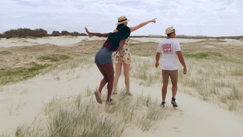 Group of friends having fun walking along sand dunes towards the beach in Australia. Wide shot on 4k RED camera.