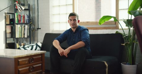 Portrait of young male professional sitting on couch in modern well lit office during the day. Wide to medium shot with soft lighting on 4K RED camera.