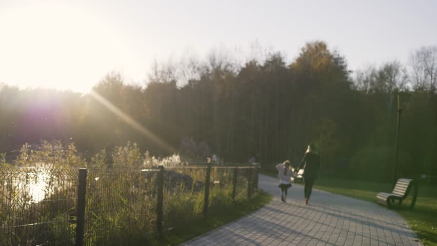 Mother walks with daughter in the Park at sunset. Light leaks. Autumn weather. Child and parent in a summer park at sunset.