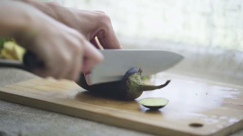Hands of woman cutting eggplant on wooden board
