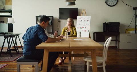 Three coworkers go over notes at meeting at wood desk in modern office during the day. Wide to medium shot with soft lighting on 4K RED camera.