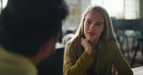 Indian male employee and female coworker have meeting at wood conference table in modern well lit design agency during the day. Wide to medium shot with soft lighting on 4K RED camera.
