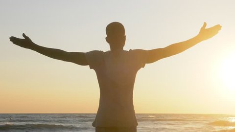 Success - silhouette of young black man opening arms at sunset at the beach.