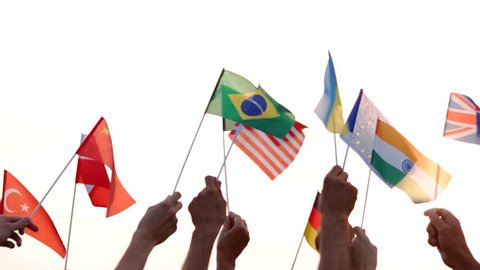 Different flags in human hands. People of different nationalities holding their countries flags outdoors. Concept of International communication.
