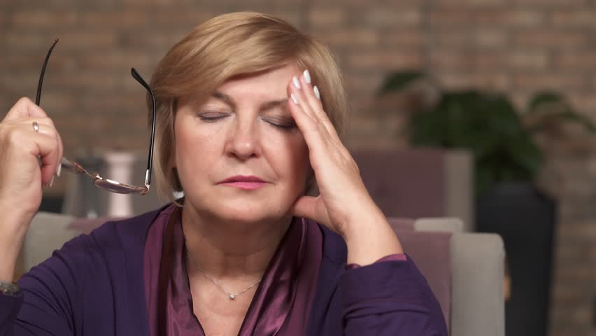 A close-up of a middle-aged woman taking off and holding glasses in her left hand. She rubs her forehead, a nose bridge, blinks eyes to rest a bit Royalty-Free Stock Footage #1018962280