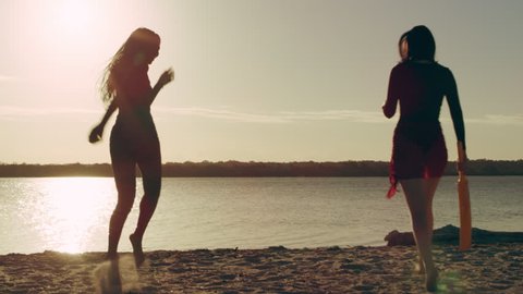 Friends running onto beach and playing cricket in silhouette with lake and sun in the background in Australia. Wide shot on 4k RED camera.