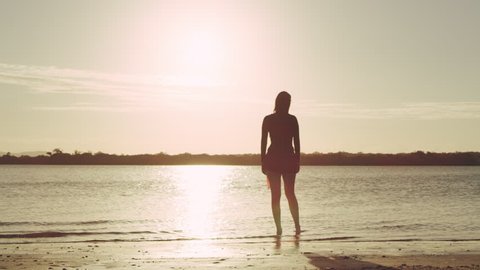 Pan across woman model standing on a beach in silhouette with lake in the background in Australia.Wide shot on 4k RED camera.