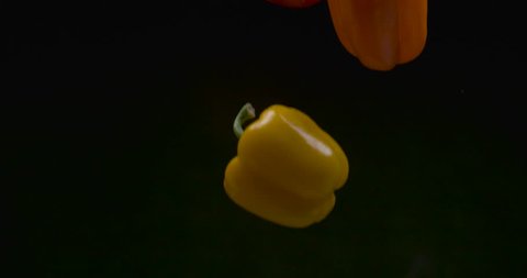 Beautiful fresh yellow, red, and orange bell peppers fall on black background closeup in ultra slow motion with 4k Phantom Flex camera.