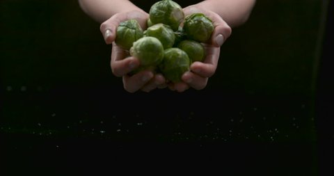 Beautiful female hands gently drop crisp brussel sprouts over water with reflection on black background closeup in ultra slow motion with 4k Phantom Flex camera.