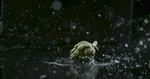 Globe artichoke beautifully drops in water and splashes over black background closeup in ultra slow motion with 4k Phantom Flex camera.
