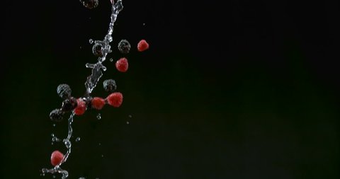 Freshly washed blueberries and raspberries fall with water droplets on black background closeup in ultra slow motion with 4k Phantom Flex camera.