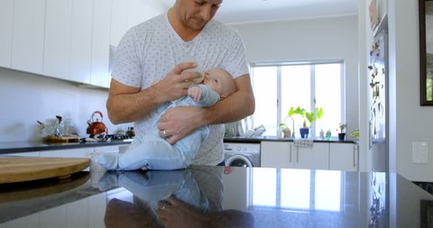 Father feeding milk to his baby boy in kitchen at home Social distancing and self isolation in quarantine lockdown for Coronavirus Covid19