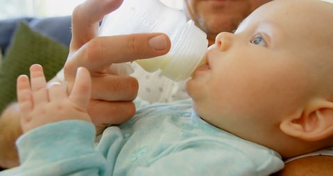 Close up of father feeding milk to his baby boy in living room at home Social distancing and self isolation in quarantine lockdown for Coronavirus Covid19